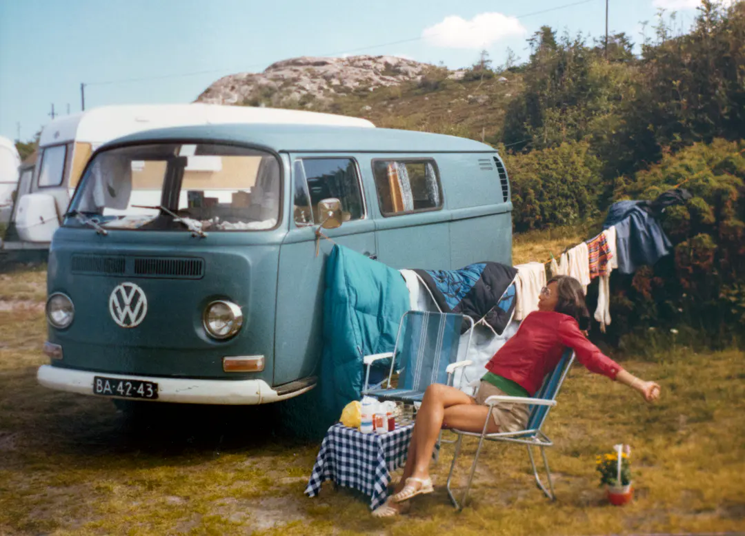 Frau entspannt neben einem Camper auf dem Campingplatz