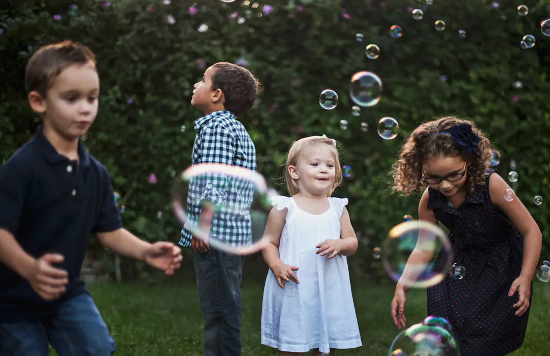 Kinder spielen gemeinsam mit Seifenblasen draußen im Garten als Beispiel für einfache Spiele ohne Material
