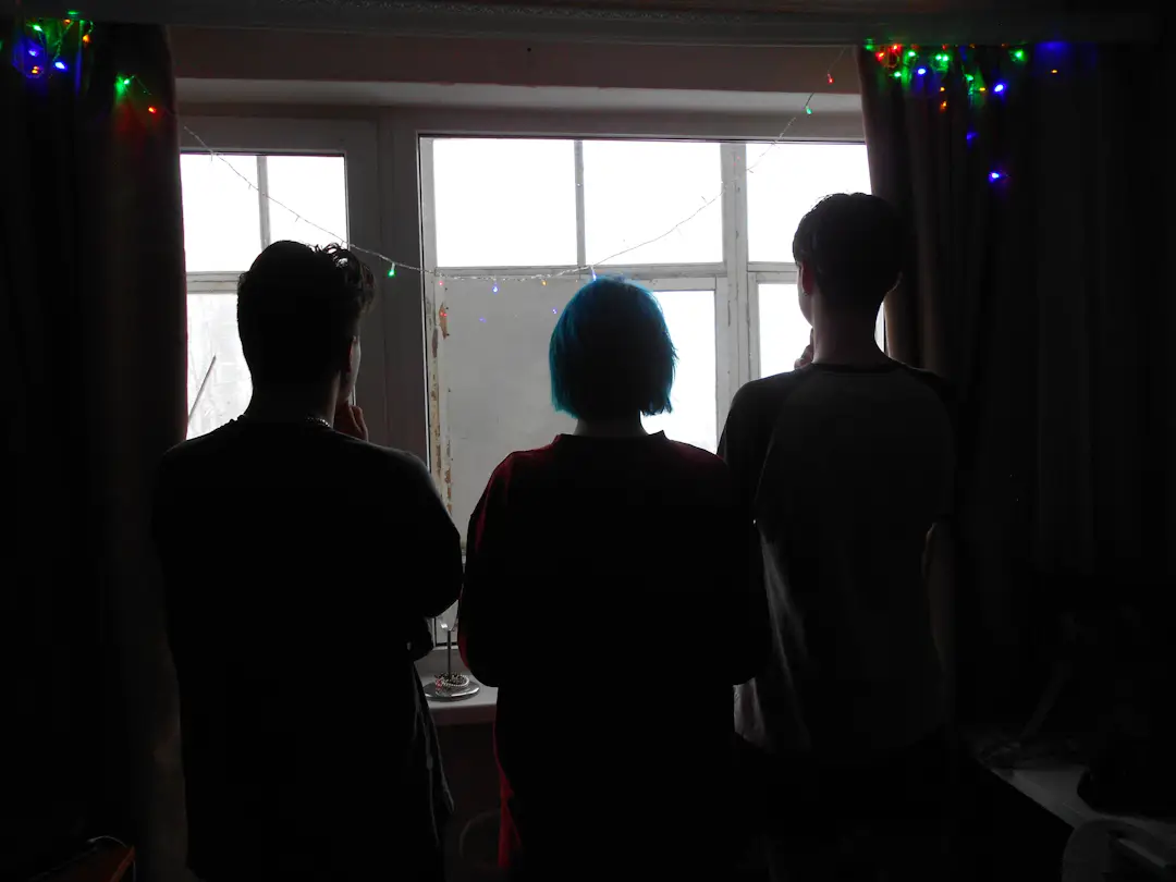 Freunde stehen an Silvester gemeinsam am Fenster und schauen auf die Lichter draußen