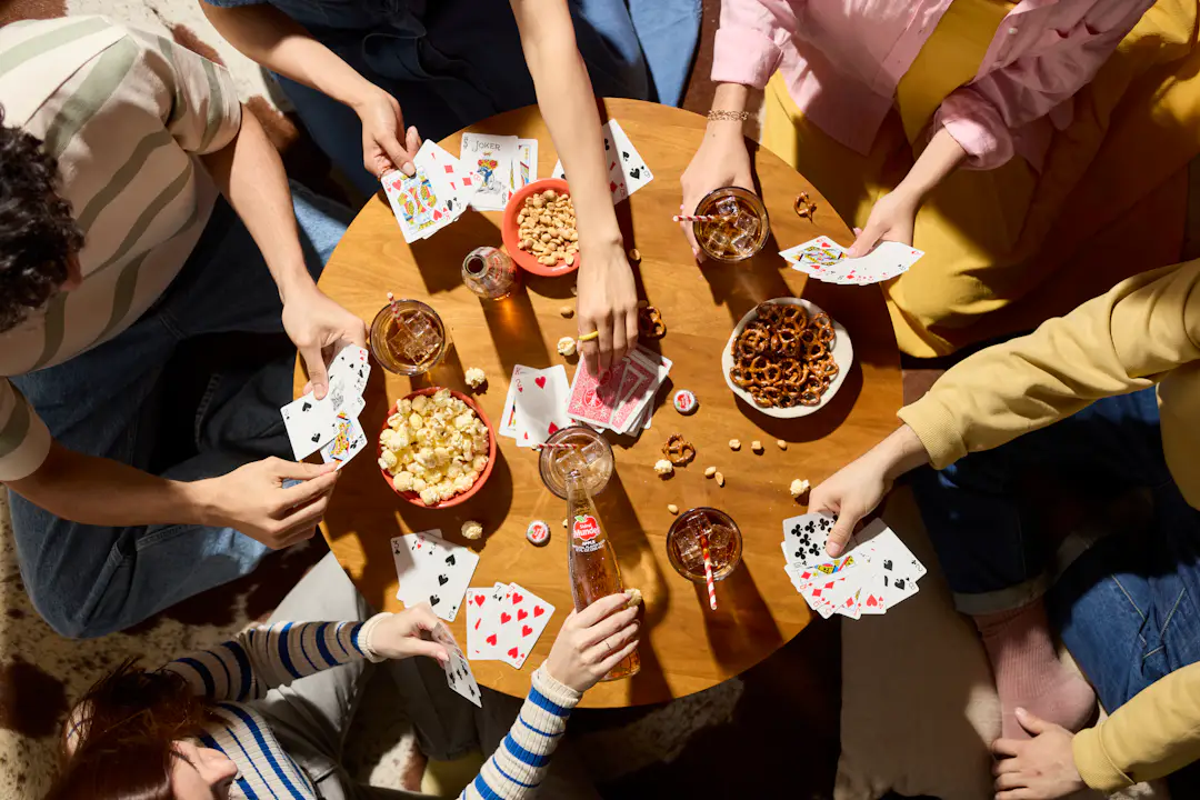 Große Freundesgruppe spielt gemeinsam Karten mit Snacks am Tisch