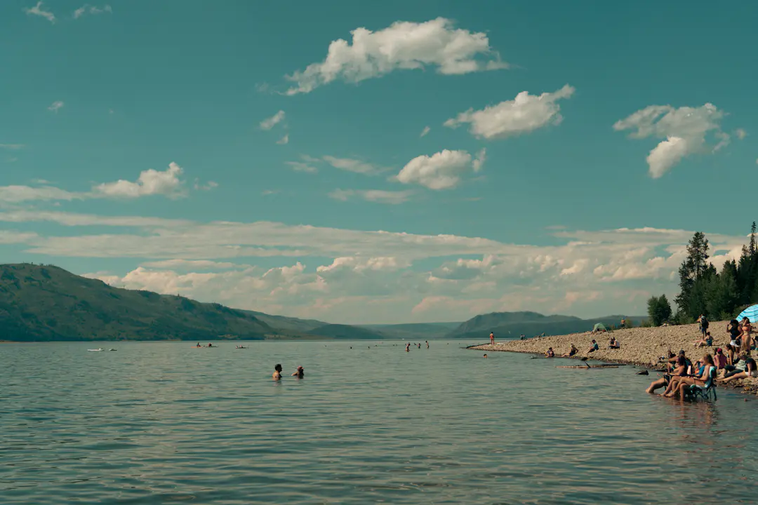 Menschen an einem ruhigen See mit Sandstrand und Bergen